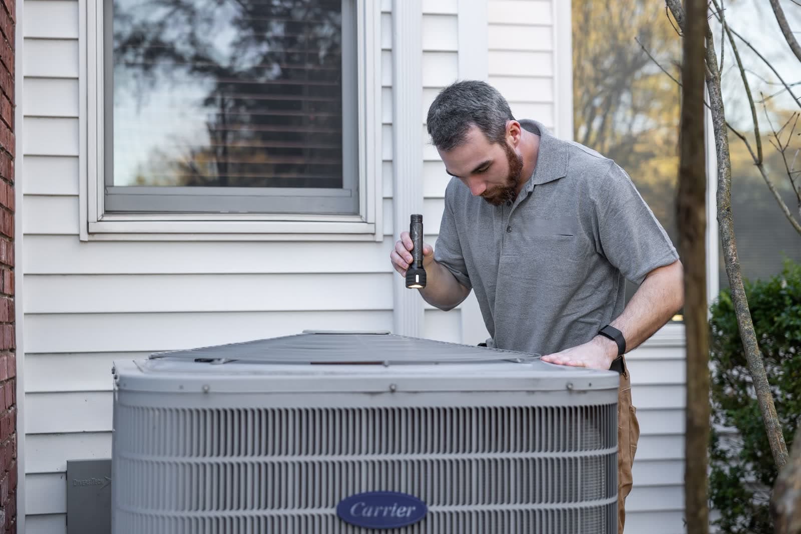 An HVAC technician works on an outdoor condenser beside a house.